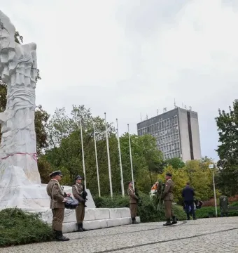 The Monument to the Battle of Monte Cassino stands in a park as soldiers gather around its base during a ceremony.