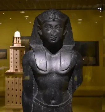 Upper portion of a Ptolemaic King statue with a headdress, damaged nose, and missing arms.