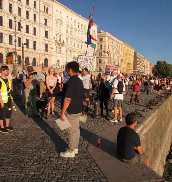 People gathered beside the Shoes on the Danube Bank memorial along a riverbank lined with shoe sculptures.