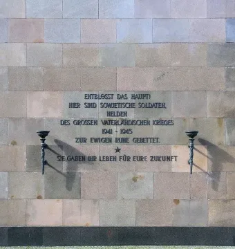 Inscribed stone wall at the Soviet War Memorial Schönholzer Heide, with torch sconces on either side of a star symbol.