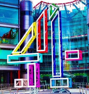 Big 4 sculpture in bright colours stands in front of a modern glass-and-steel building.