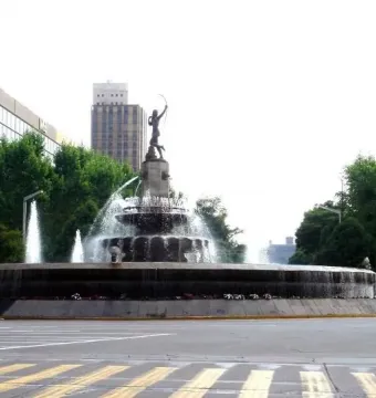 Diana the Huntress Fountain with a tall statue and water spraying from a multi-tiered stone base at a city intersection.
