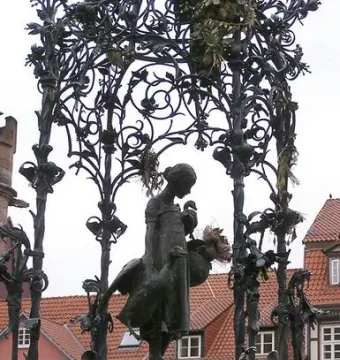 Gänseliesel Fountain with a bronze girl holding two geese on a stone pedestal beneath an ornate metal canopy.