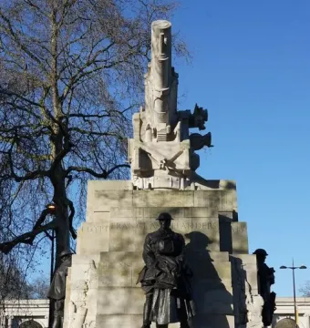 The Royal Artillery Memorial with a stone howitzer sculpture and bronze soldier figures on the base against a blue sky.