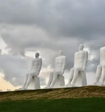 The Man by the Sea sculpture with four white seated figures on a grassy hill under a cloudy sky.