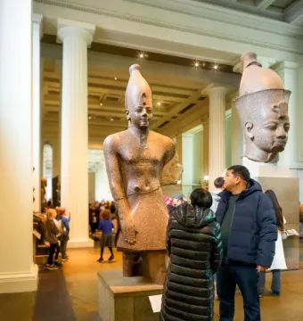 Colossal head of Amenhotep III displayed in a museum hall beside a separate ancient Egyptian torso fragment.