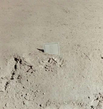 Fallen Astronaut memorial showing a small white astronaut figure lying on a dusty surface beside a partially embedded plaque.