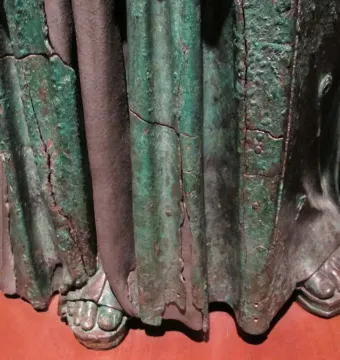 Lower section of Minerva d\'Arezzo showing weathered drapery and sandals on a reddish-brown base.