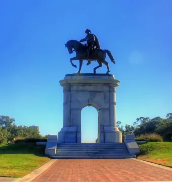 Sam Houston Statue on a stone archway with a rider on horseback above a grassy knoll and brick walkway.