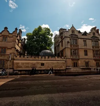 The Shelley Memorial’s dark ribbed dome tops a stone wall between ornate university buildings, with a small plaque below.