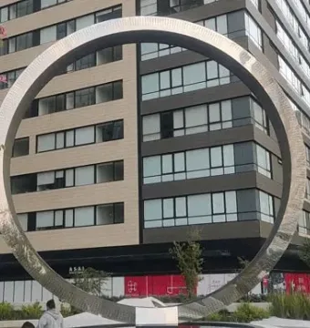 The Eye of Mexico circular metal sculpture framed against tall residential buildings.