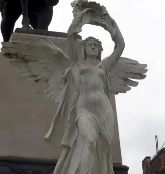 Bartolomé Mitre Monument featuring a winged allegorical figure holding a leafy wreath before a tall stone pedestal.