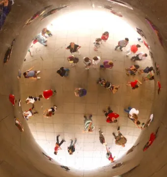 Crowd reflections distorted on Cloud Gate\'s polished concave surface.