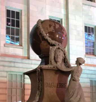 Daguerre Memorial stone sculpture with a bust of Daguerre, a large globe, and a draped female figure with a laurel garland.