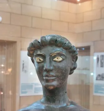 Close-up of the head and upper chest of the Efebo de Selinunte bronze statue with inlaid eyes and curly hair.