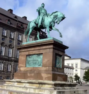 Frederick VII equestrian statue on a tall stone pedestal in a city square.