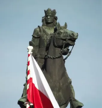 The Grunwald Monument shows a crowned armored rider on horseback against a clear blue sky, with a Polish flag in the foreground.