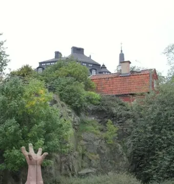 La Mano stone sculpture of an upright hand beside a roadway, with a rocky hillside and trees behind it.