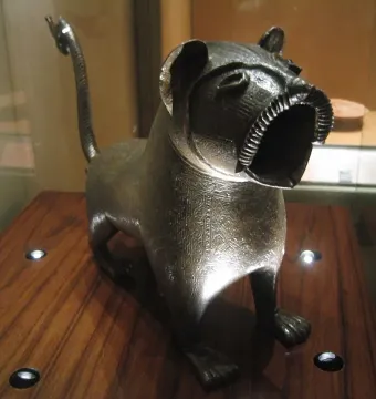 Lion of Monzon sculpture with a curved articulated tail, shown on a wooden surface.