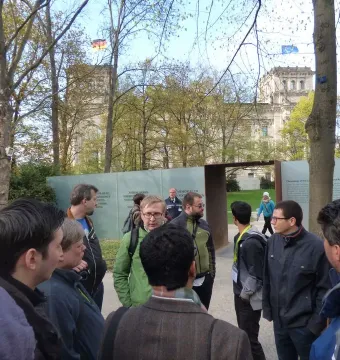 Translucent text panels and a dark metal gateway at the Memorial to the Murdered Sinti and Roma of Europe, with people gathered nearby.
