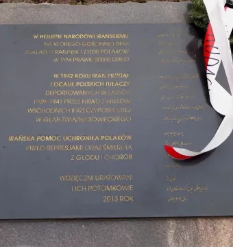 Dark grey plaque on the Monument of Gratitude to the Iranian People with gold Polish and Persian inscriptions and a white-and-red ribbon draped over one side.
