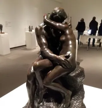 The Kiss bronze sculpture showing two nude figures embracing on a rocky base in a museum gallery.