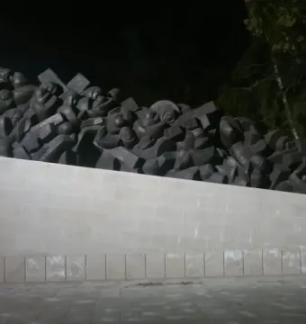 The Train of Pain monument at night, showing a dark sculptural mass of stylized figures on a long stone base.