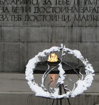 Unknown Soldier Monument with an eternal flame beside a snow-covered metal wreath and stone wall inscription.