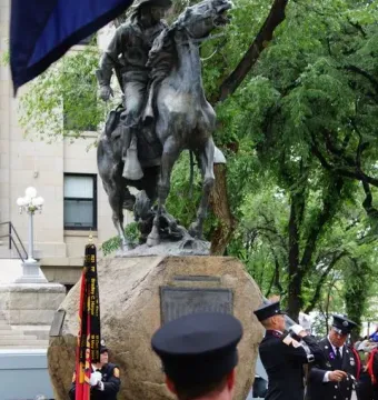 Buckey O\'Neill Monument, an equestrian bronze statue on a rock base, with uniformed people gathered below and a ceremonial flag in front.