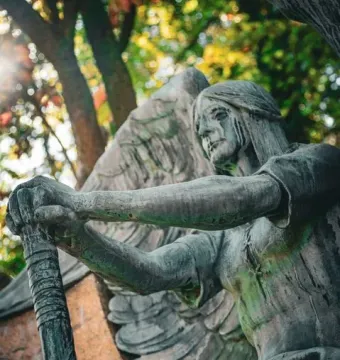 The Haserot Angel statue holding an upside-down torch, with dark streaks on its face and feathered wings behind it.