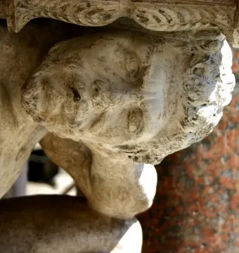 Close-up of Il Gobbo di Rialto showing the weathered stone head and hunched upper body beneath an ornate carved structure.