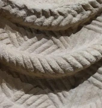 Close-up of light-colored stone relief carving with braided curved bands and woven patterns from the Lady of Cerro de los Santos.