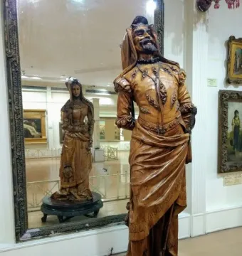 Mephistopheles and Margaretta sculpture with a bearded man in elaborate attire and a woman reflected on the reverse side in a mirror.