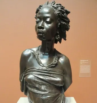 The Nubian Woman bronze bust with tightly coiled hair, a beaded necklace, and a draped garment across the chest.