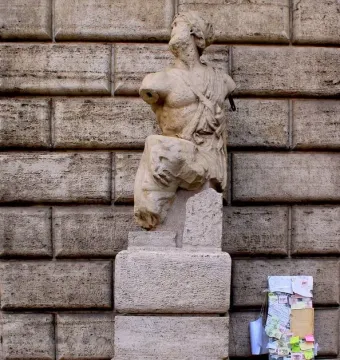 Pasquino, a weathered stone statue on a pedestal beside a post covered with handwritten notes.