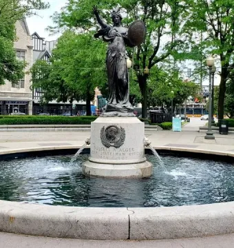 Russell Alger Memorial Fountain with a bronze female statue atop a circular fountain in a paved plaza.