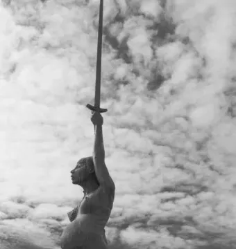 Verity, a bronze sculpture of a pregnant woman holding a sword aloft against a cloudy sky.