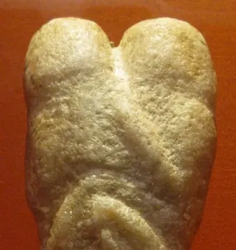 Ain Sakhri Lovers stone carving with intertwined rounded forms against a reddish-orange background