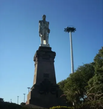 Monument to General Carlos M. de Alvear on a dark pedestal, with a tall white pole and trees beside it.