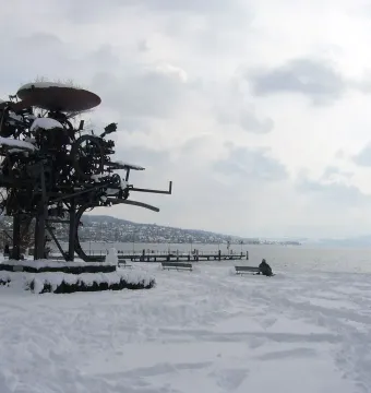 Heureka, a dark metal sculpture of wheels and gears in a snowy lakeside park.