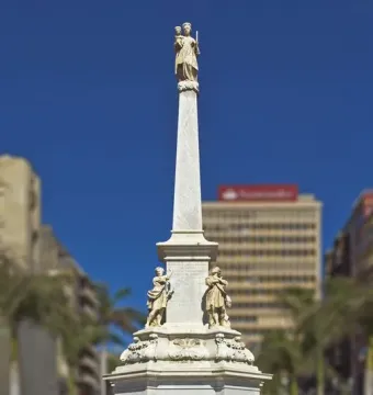Triumph of the Candelaria obelisk with a small figure at the top, surrounded by a low fence against a blue sky.