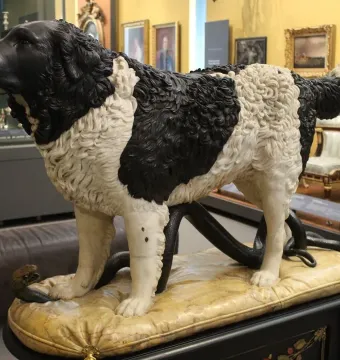 Bashaw sculpture of a dog standing over a coiled snake on a carved cushion.