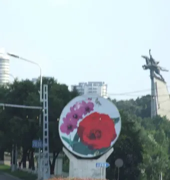 The Chollima Statue appears as a dark silhouette on a tree-covered hill against a bright hazy sky.