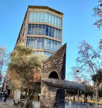 Monument to Narcís Monturiol with a dark angular sculpture and a submarine-shaped vessel on a city sidewalk.