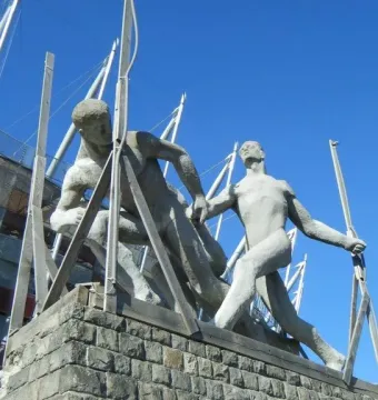 Sztafeta sculpture showing two stone runners in a relay handoff near a stadium.