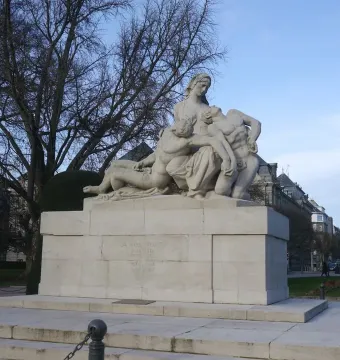 Stone war memorial with a central female figure cradling two other figures on a tiered base with inscriptions.