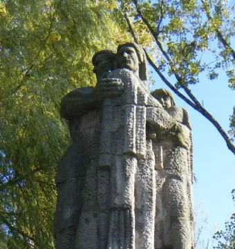 Weathered stone monument with three figures and the inscription \