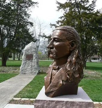 Wild Bill Hickok Memorial bronze bust on a stone base beside a granite boulder plaque in a grassy park