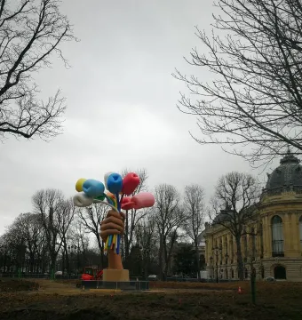 Bouquet of Tulips sculpture showing a brown hand holding colorful, balloon-like tulips in a park with trees and a domed building behind it.