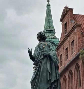 Nicolaus Copernicus Monument in Toruń, a bronze robed figure pointing upward with a celestial sphere in hand.